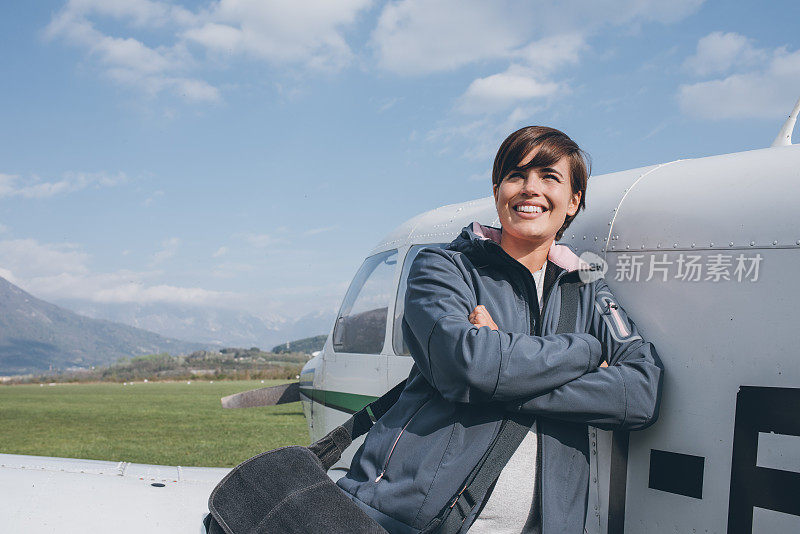 微笑的女飞行员与她的飞机摆姿势