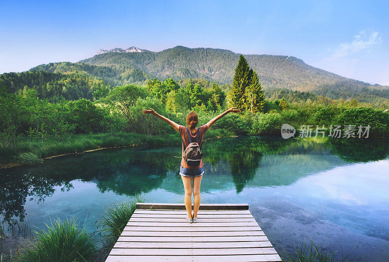 一名年轻女子站在木桥上，双手高举，背景是大自然。