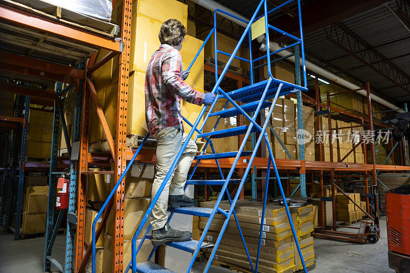 一名男性仓库工人正确地爬上滚动梯子。