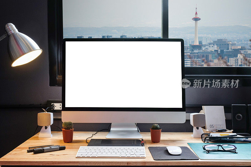 平面设计师的工作空间配备了一个手写板，一台电脑和白色的文本屏幕与美丽的日落从窗口山