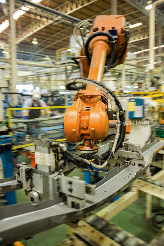 在工厂里，机器人手臂和手柄将汽车部件固定在滚筒输送机上