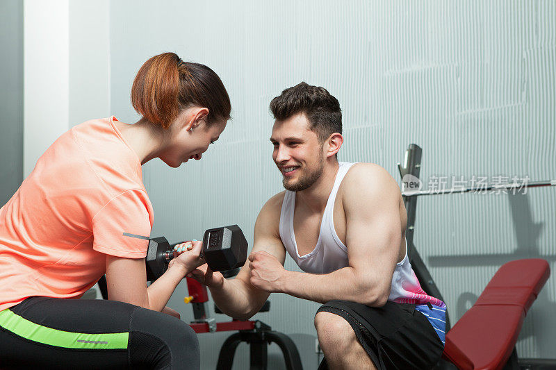 男教练在健身房帮助女教练训练