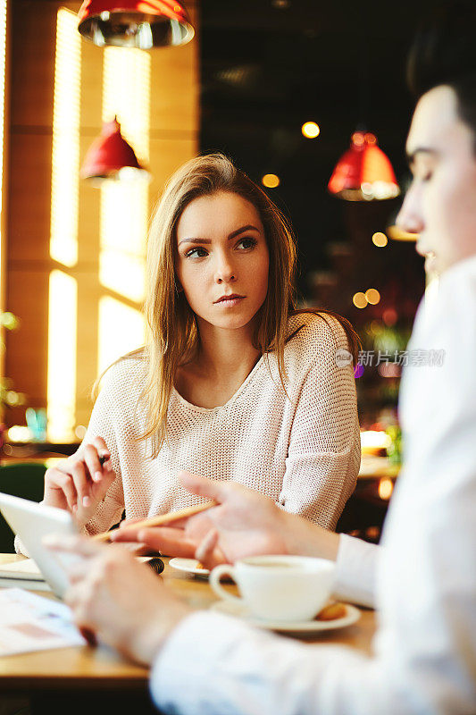 一个自信的女人和她的男同事坐在咖啡馆里分享平板电脑，讨论上面的数据