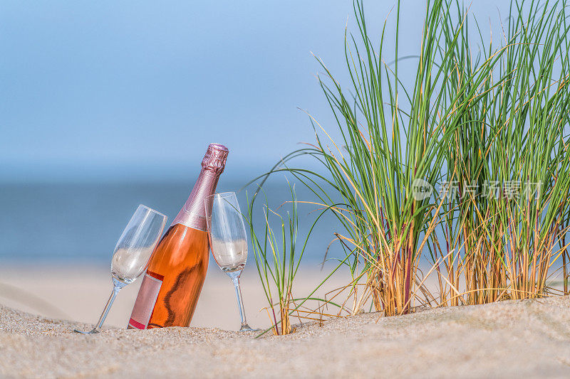在沙滩上的沙滩上，两个酒杯和一瓶玫瑰香槟
