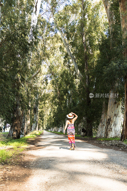 快乐的女人走在两旁长满树的路上。