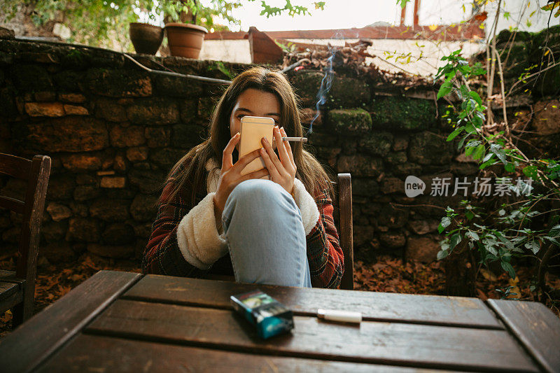 看起来友好的智能手机年轻女子坐在咖啡馆拿着烟和吸烟