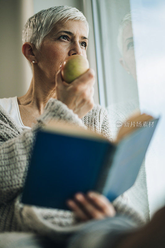 下图是一个成熟的女人在窗边边吃苹果边看书。