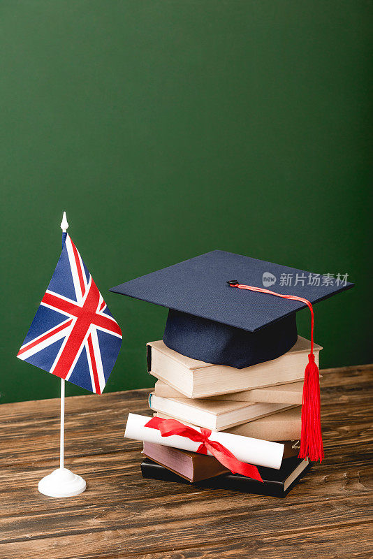 书籍、学术帽、文凭和英国国旗木质表面上绿色