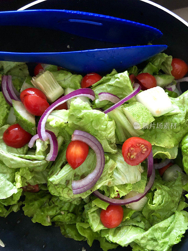 Stock形象的健康高蛋白沙拉食物作为减肥午餐在一个碗与塑料服务钳子，健康的绿色沙拉与生菜叶，红洋葱，西红柿随时食用，健康的饮食习惯