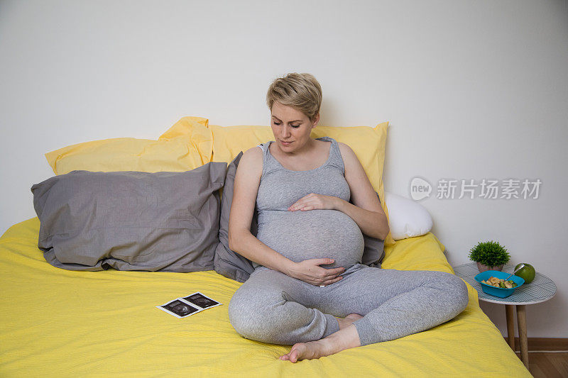 幸福的微笑孕妇躺在床上，触摸她的肚子在家里