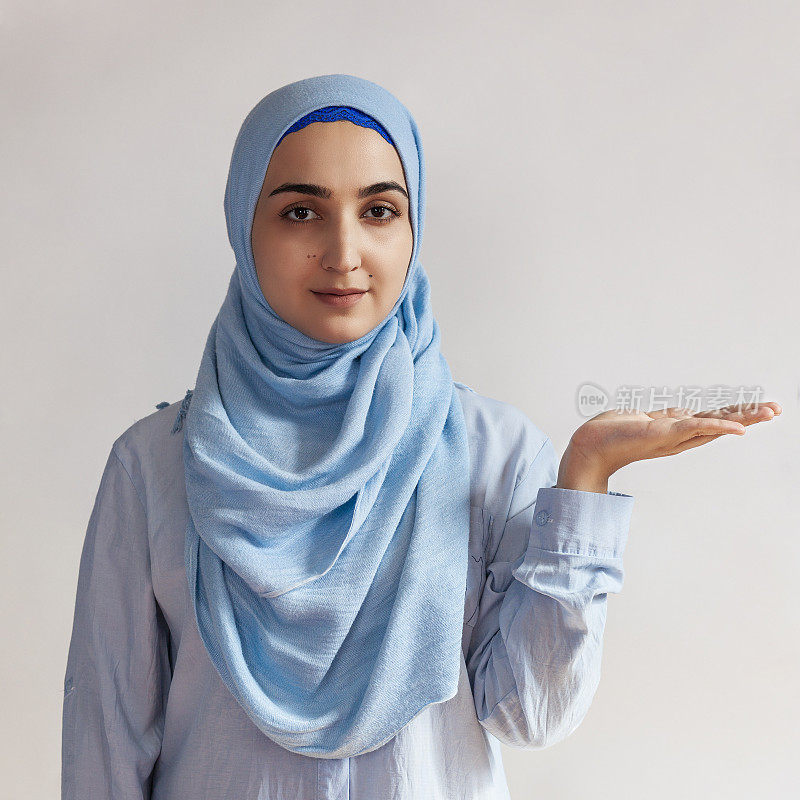 可爱的穆斯林妇女戴着头巾的肖像。为文本复制空间。美丽的穆斯林女孩举起手掌在复印空间，好像拿着什么东西