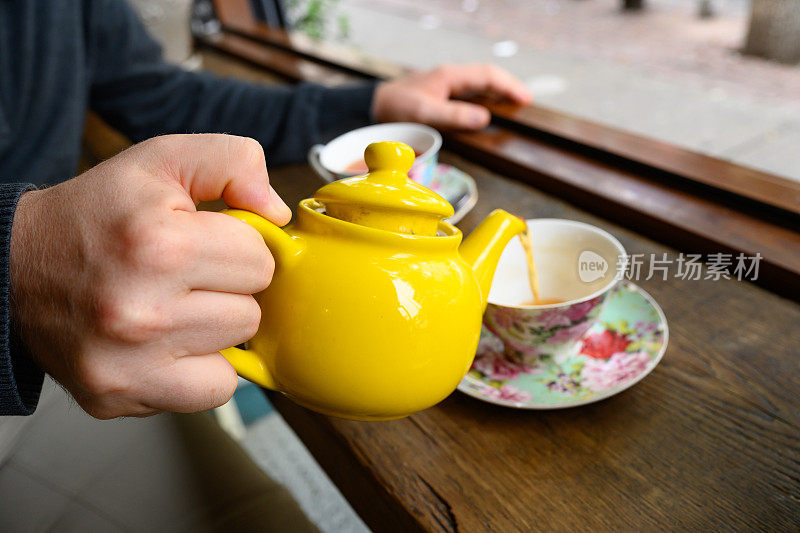 在布鲁克林的一家咖啡馆里，一名男子将茶壶里的热茶从一个黄色水壶里倒入花杯