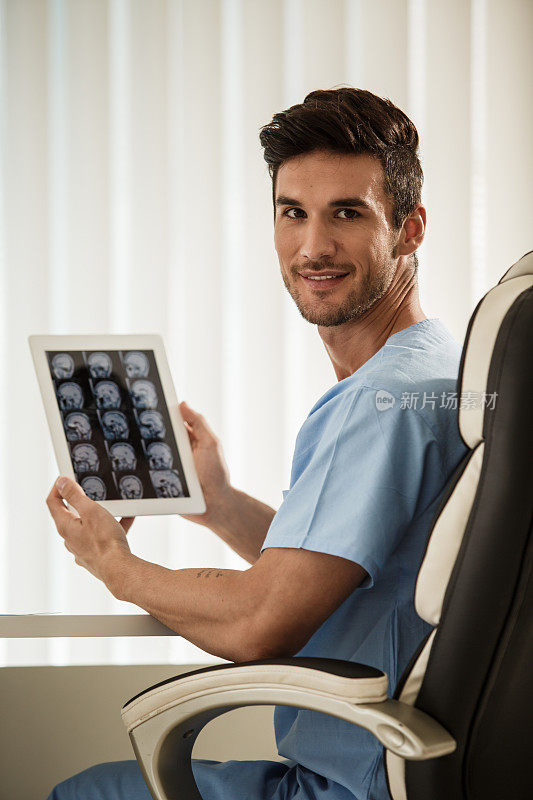 一名男性外科医生手持电子平板电脑，屏幕上显示着脑瘤的核磁共振扫描图