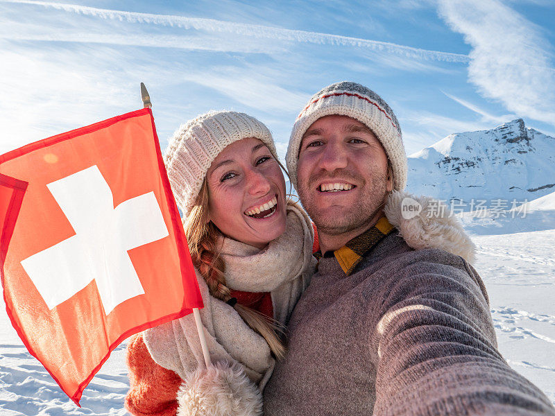 一对夫妇在瑞士阿尔卑斯山白雪皑皑的山上与瑞士国旗自拍