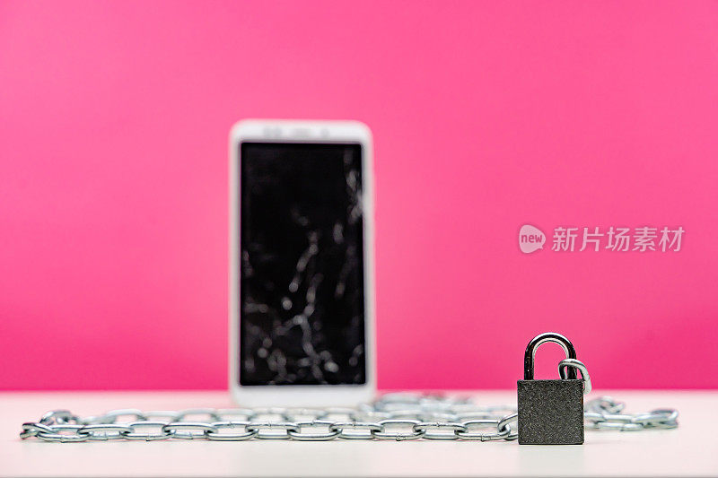 粉色背景上用挂锁和链条锁着的坏掉的智能手机