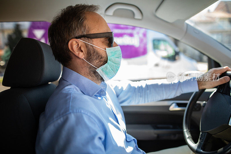 成熟的男子坐在汽车上戴着外科口罩，以防止病毒