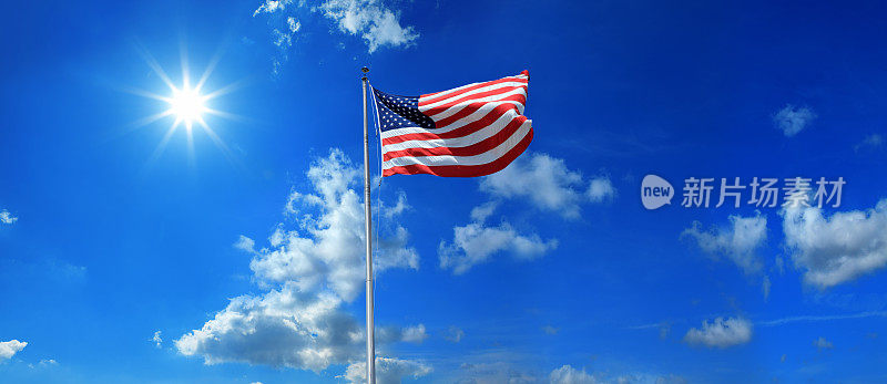 在晴朗的蓝天和灿烂的阳光下，旗杆上挂着美国国旗