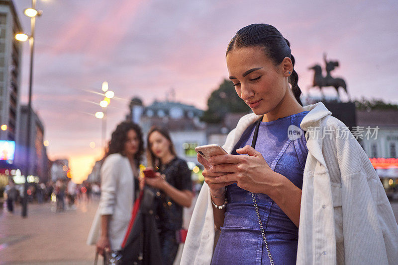 性感的年轻女子使用手机在一个城镇广场在日落