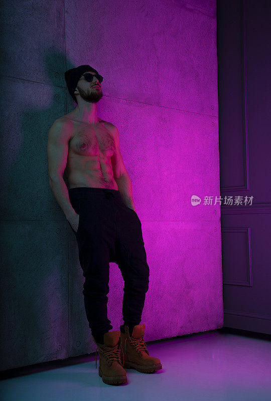 全身肖像的一个健康的野蛮的年轻人赤裸上身在工作室与紫色霓虹灯的颜色摆姿势。