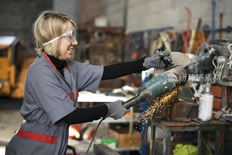 妇女在仓库里使用锯子。侧视图和切割铁件微笑