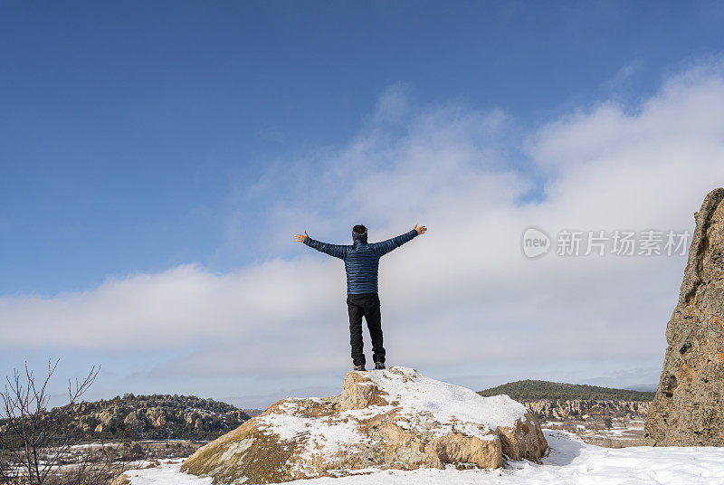 一个徒步旅行者站在白雪覆盖的山顶上，举起双臂庆祝他的成功