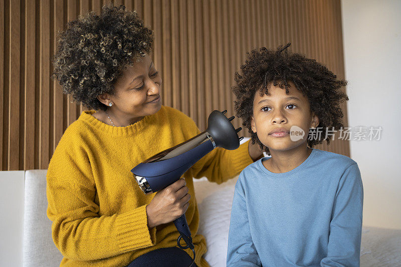 非洲裔母亲在卧室里用吹风机吹干儿子的头发