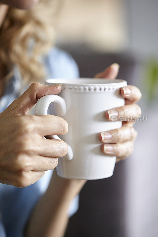 女人的手握白色的咖啡在办公室白天的特写