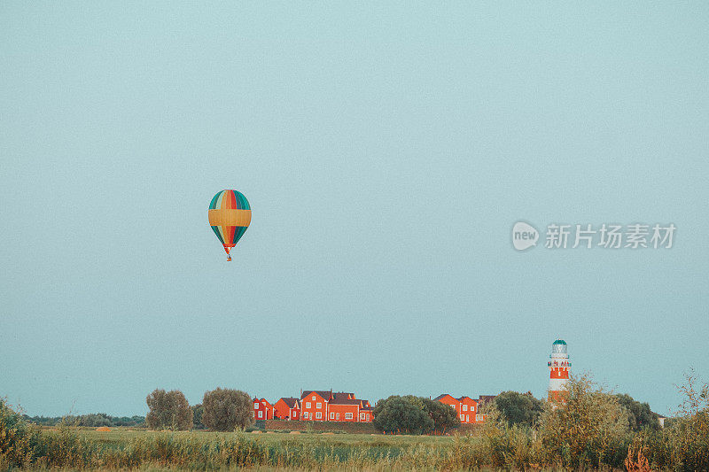 在傍晚的灯光下，气球在一个有红房子和灯塔的村庄附近飞行