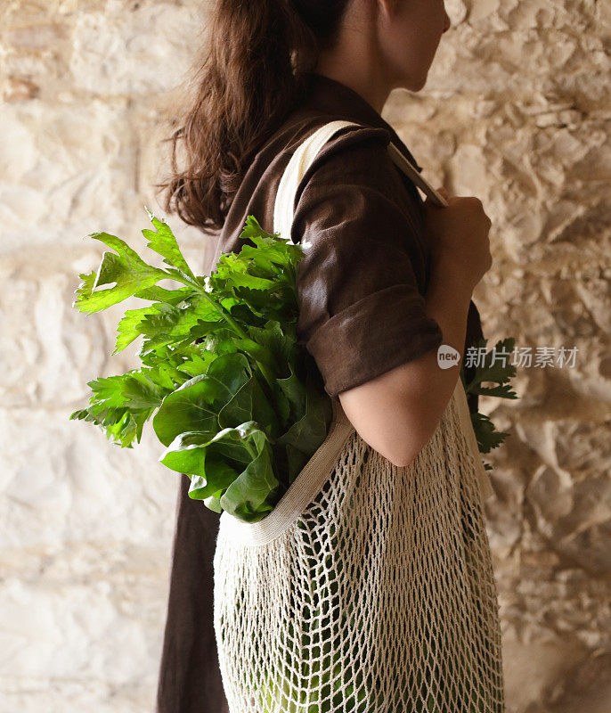 女人拿着网袋，里面装着绿色蔬菜和香草