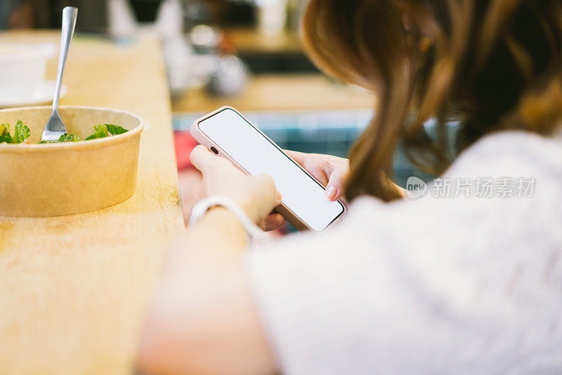 一个女人在咖啡馆里用手机看书、发短信、看视频、浏览社交网络、做笔记、网上购物。比尼斯女士在午餐时间使用智能手机。