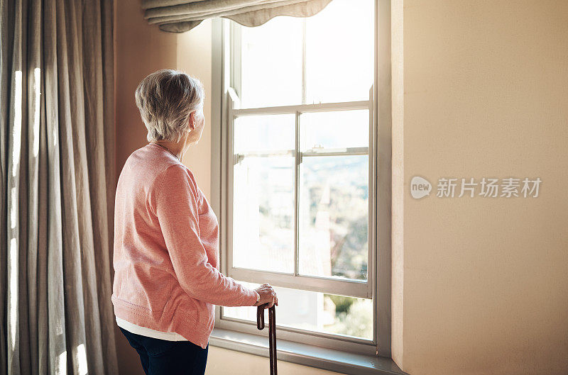 一位老妇人拄着拐杖，若有所思地看着窗外