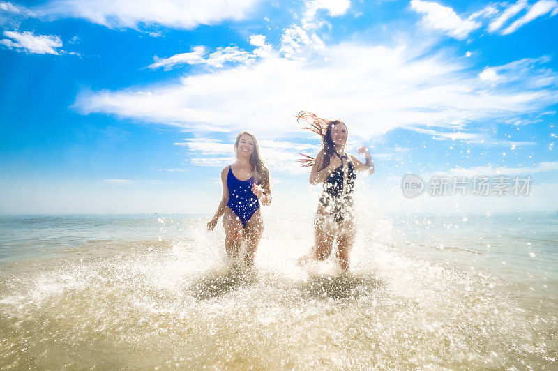 阳光明媚的沙滩上，两个穿着泳衣的年轻女子在海里嬉戏奔跑，嬉水嬉戏