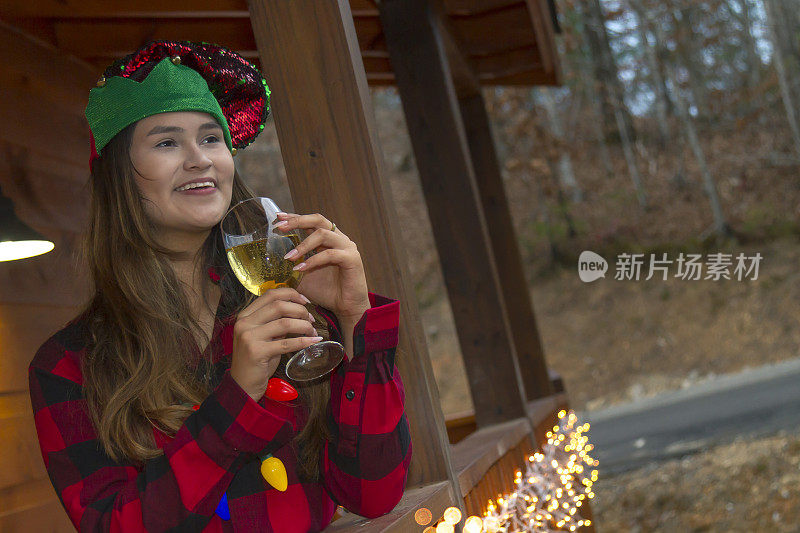 这是一个拉丁少女的肖像，在圣诞节的前几天，她在家外面感觉着美好的气味，喝着香槟，穿着冬季圣诞服装，在美国的森林中享受一个轻松寒冷的下午。