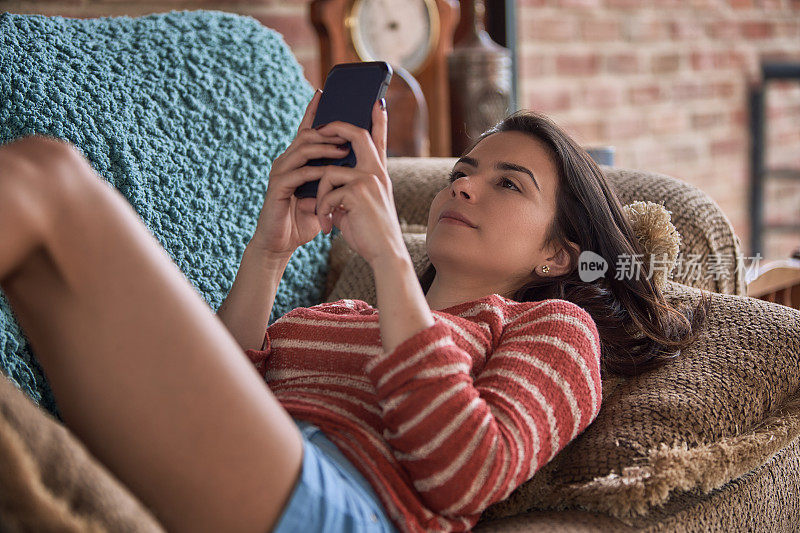 西班牙年轻女子躺在沙发上使用智能手机