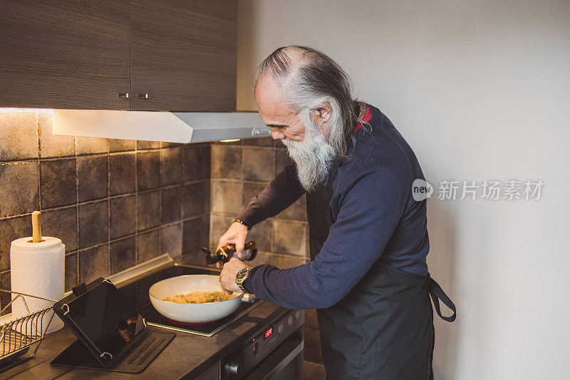 一名留着长胡子的成年男子通过数字平板电脑观看烹饪教程