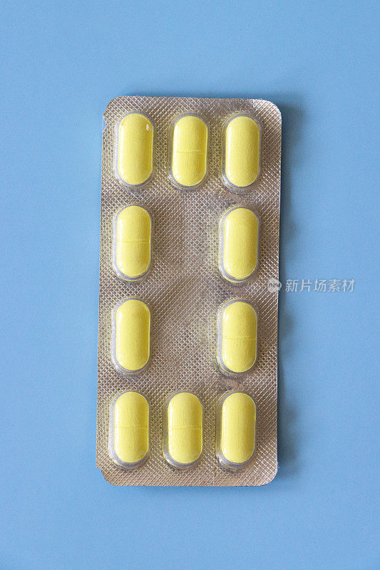 特写图像个人银背制药片剂泡罩包，一排排黄色胶囊药物可见通过透明塑料口袋，蓝色背景，上升的观点