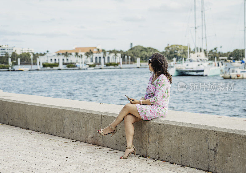 一个拉丁女人在热带地区的海滨码头上用手机