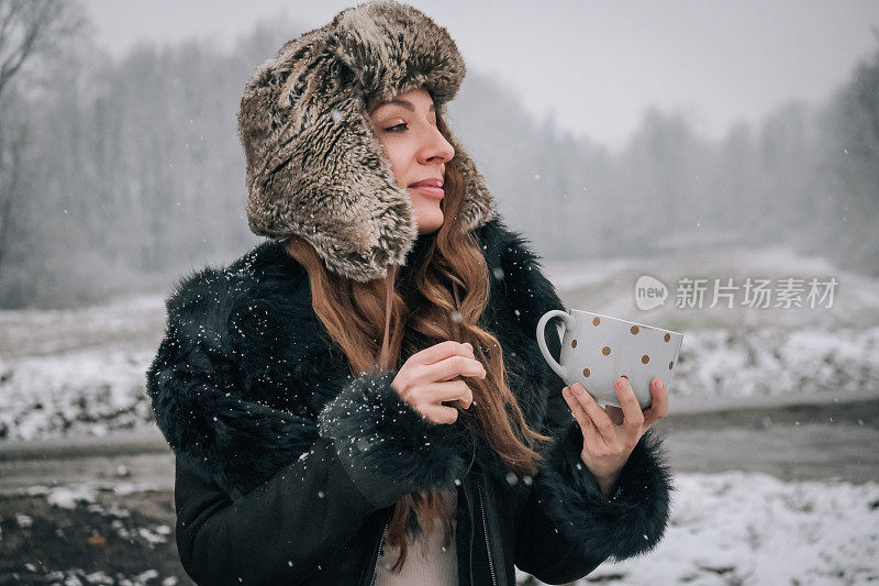 站在雪地上拿着一杯茶的年轻女子