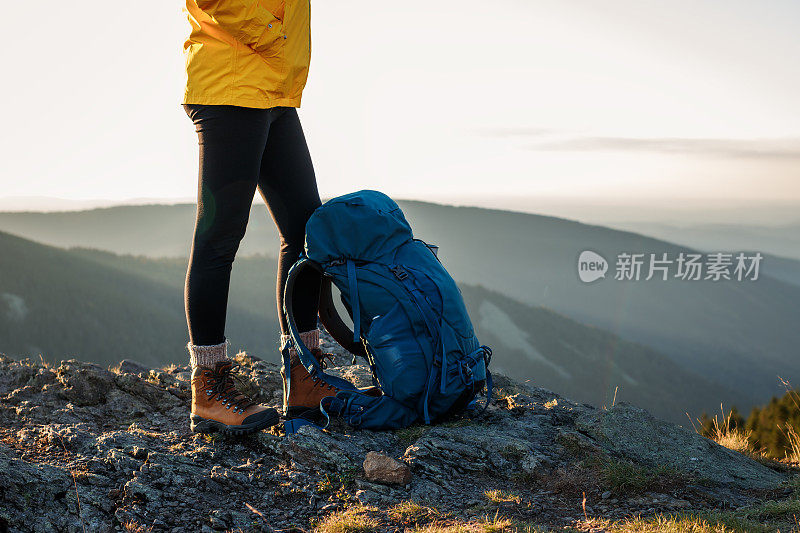 背包和登山靴的徒步旅行者爬上山顶后，站在岩石上