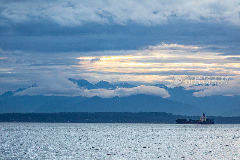 货船在美丽的风景优美的海港在黄昏云在天空山脉的背景