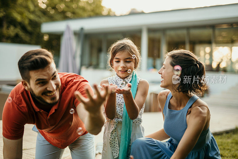 一个快乐的家庭沉浸在团聚的魔力中，父母和女儿在他们迷人的住所外快乐地玩耍