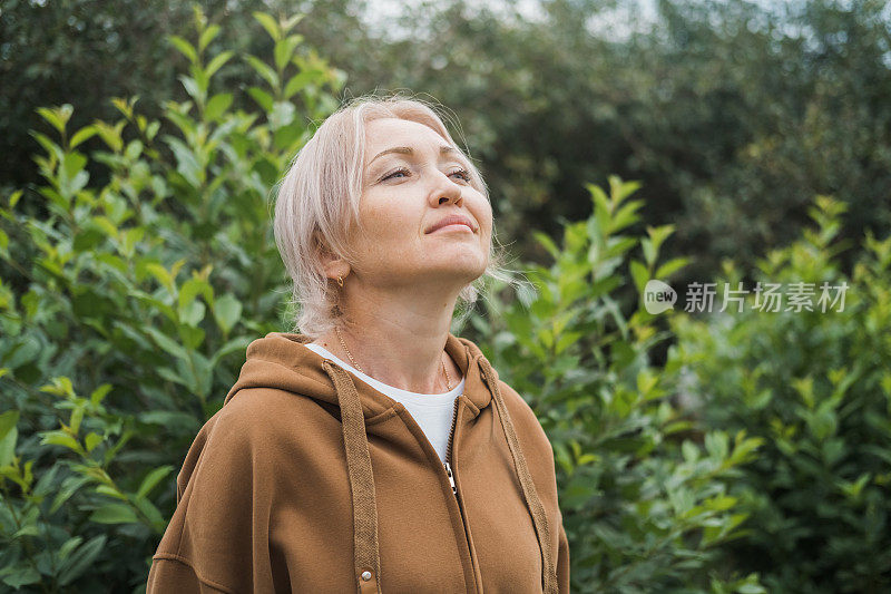 一个放松的白人妇女在绿色的森林里呼吸新鲜空气的肖像。