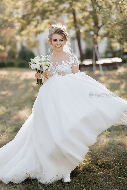 一位金发碧眼的新娘身穿白色长裙，手拿花束，面带微笑地走着