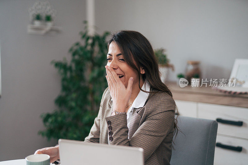 在现代家庭办公室里，一位年轻的女商人在办公桌前工作时看起来很无聊