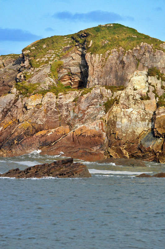 风景优美的大自然-宁静的垂直场景的海水波浪旁边的悬崖，岩石或石头在海滩上的浅蓝色的天空与陆地合并在地平线上，德文郡，英格兰，英国