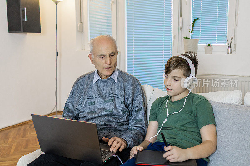 爷爷和孙子坐在家里的沙发上使用笔记本电脑。
