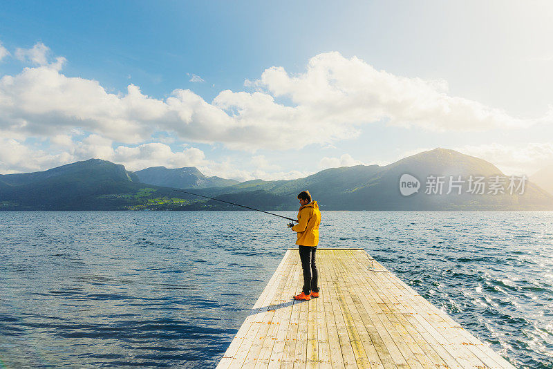 夏天在挪威峡湾与山景钓鱼的黄夹克男子