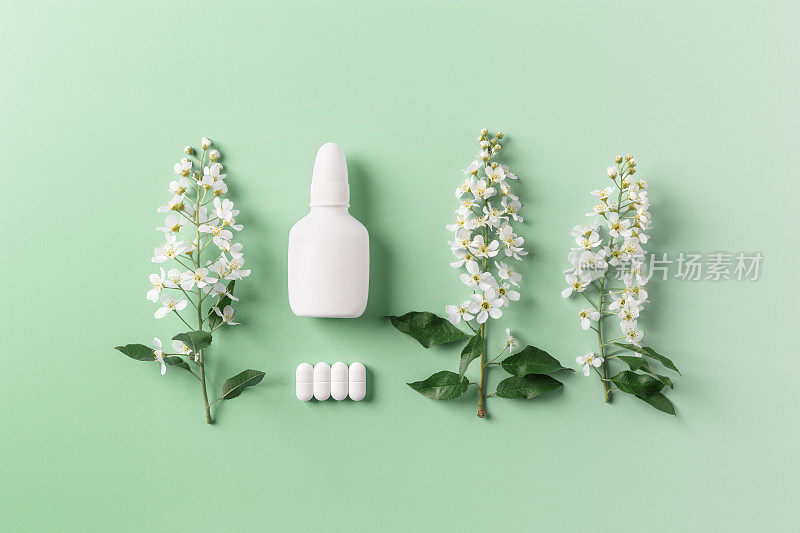 季节性的春季过敏，春天的树枝树上有鲜花和鼻腔喷雾剂的模拟瓶，药丸上绿色的背景，过敏的概念开花。抗组胺喷雾剂用于鼻塞