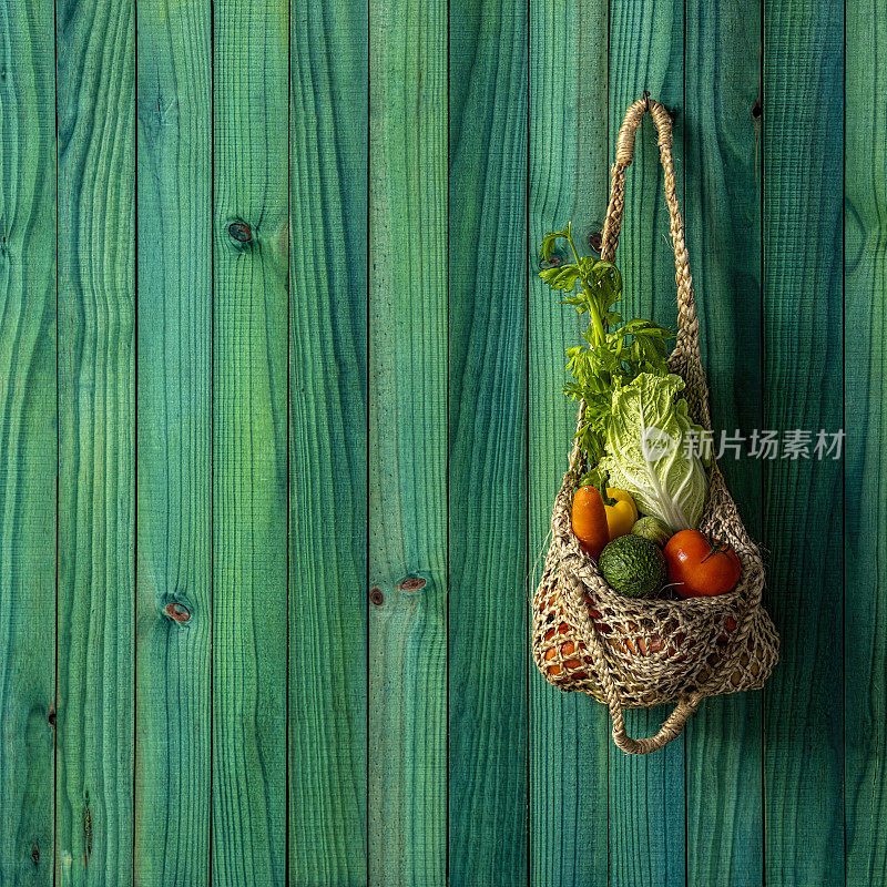 色彩缤纷的市场新鲜什锦蔬菜在一个天然棉花可重复使用的购物袋挂在一个充满活力的绿松石色木制墙板背景。