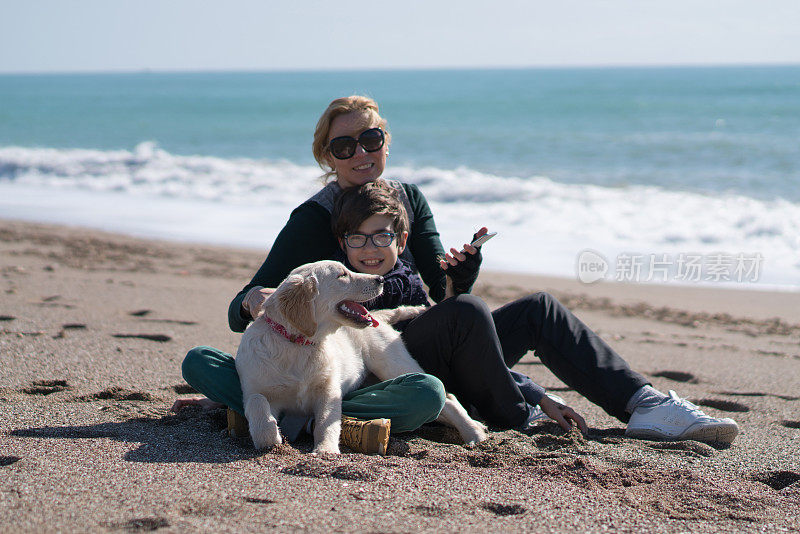 妈妈和儿子和她的狗坐在海滩上